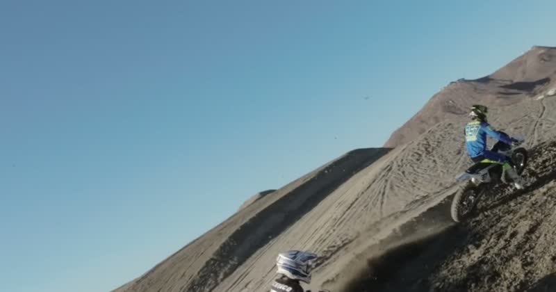 4K aerial frame of a rider cresting a hill face against open sky.